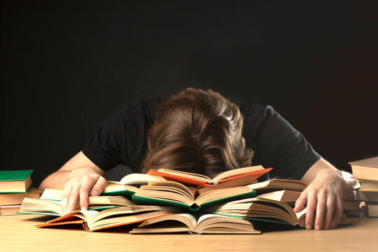 Person ligger utslått med hodet i en haug av bøker